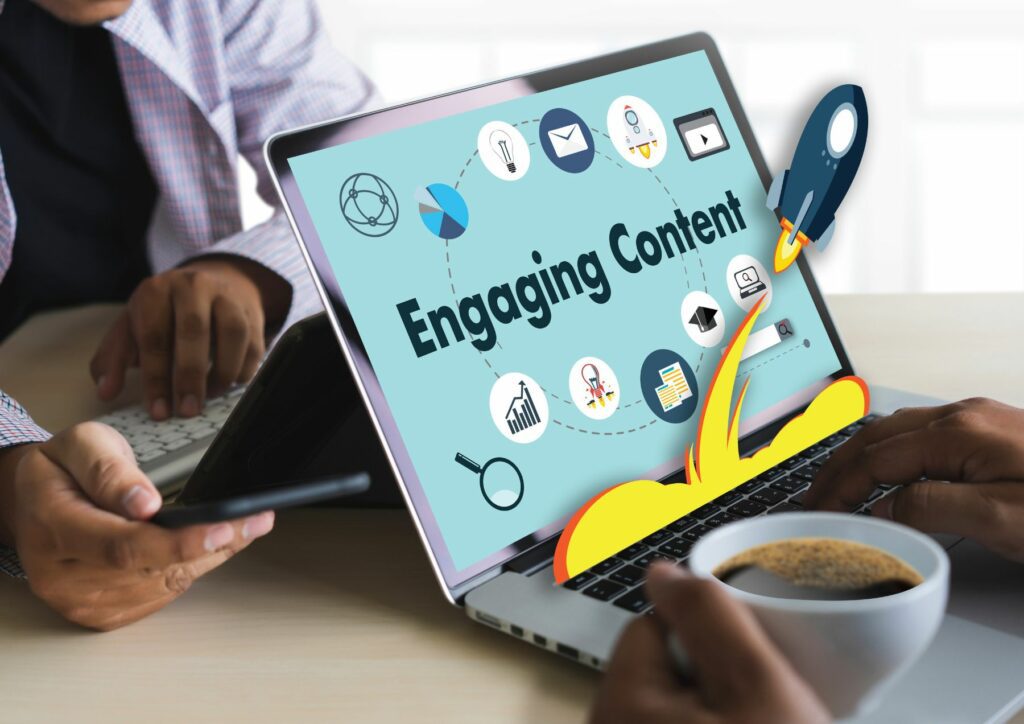 Two people sitting down the table, one is using their laptop displaying the word "Engaging Content" and icons related to e-commerce at the sides.