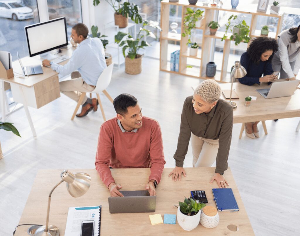 Am office environment with people working together in pairs and in solo as they are working in front of their desktops and laptops.